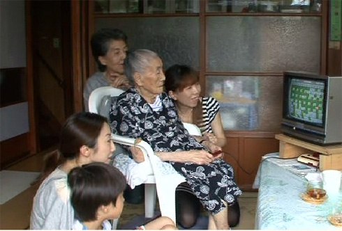 99 year old Umeji Narisawa plays her favorite videogame while her family watches